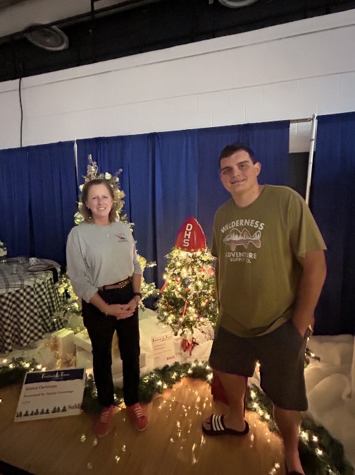 A person and person standing in front of a christmas treeDescription automatically generated